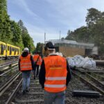 Menschen in Warnweste laufen über Schienen auf einer Baustelle