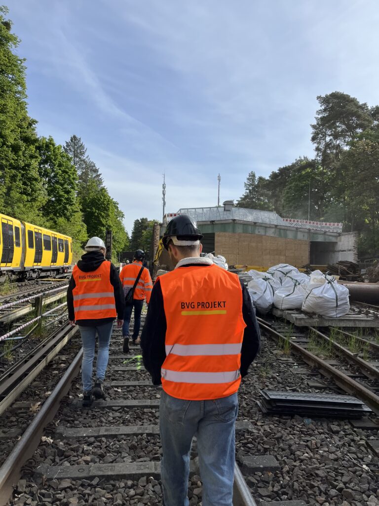 Menschen in Warnweste laufen über Schienen auf einer Baustelle