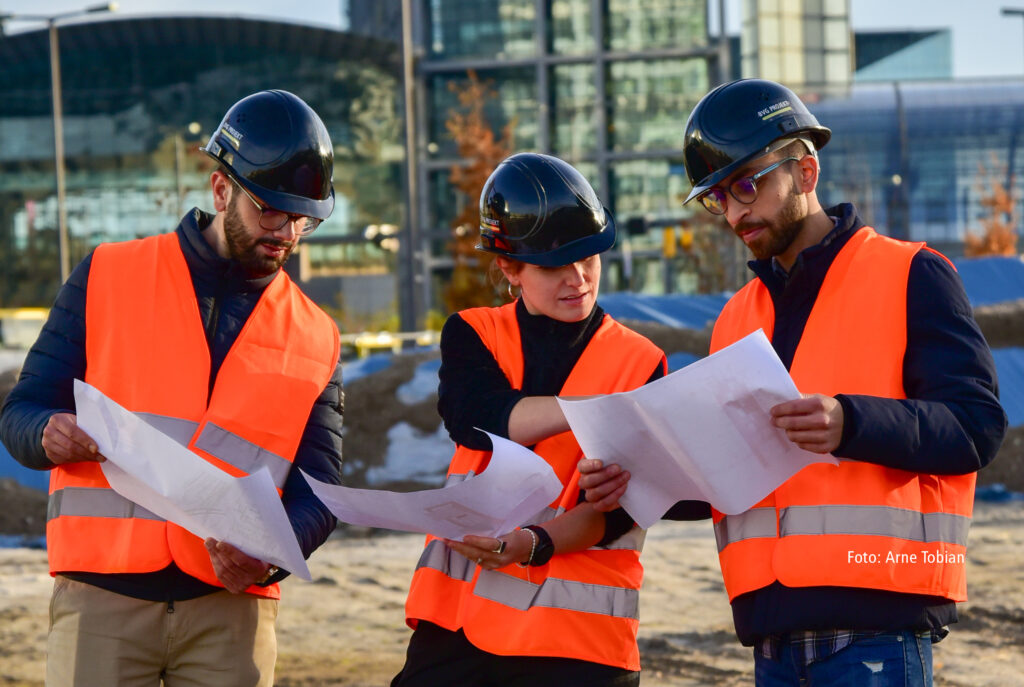 drei Personen in Warnweste beraten auf der Baustelle